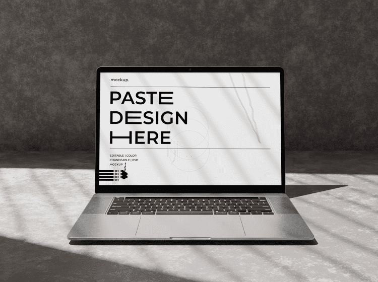 Portfolio-Img-2png - Corporate video production company in Delhi Laptop on a concrete surface showing a design mockup on the screen with the words 'PASTE DESIGN HERE' in bold black letters.