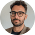 Story-1png - Corporate video production company in Delhi Portrait of a man with glasses and a beard, looking at the camera against a green circular background.